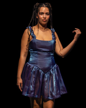 Model wearing a blue dress on a dark runway with an audience.